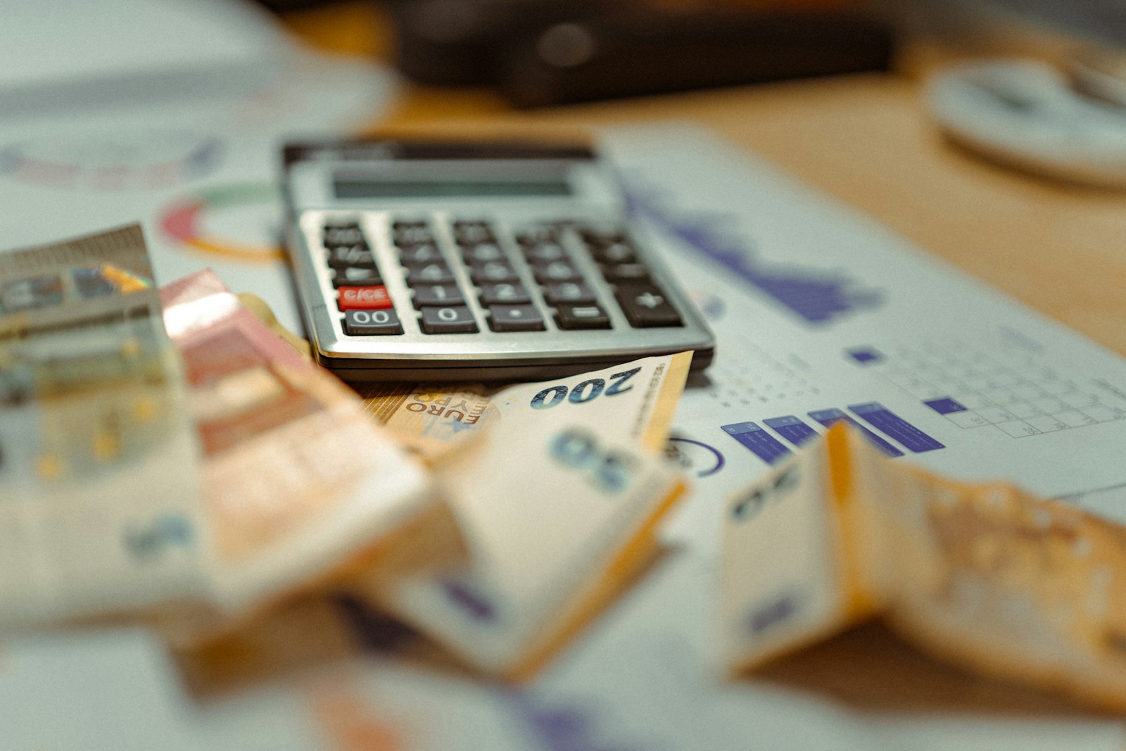 Kalkulator leżący na banknotach i wykresach na drewnianym biurku
